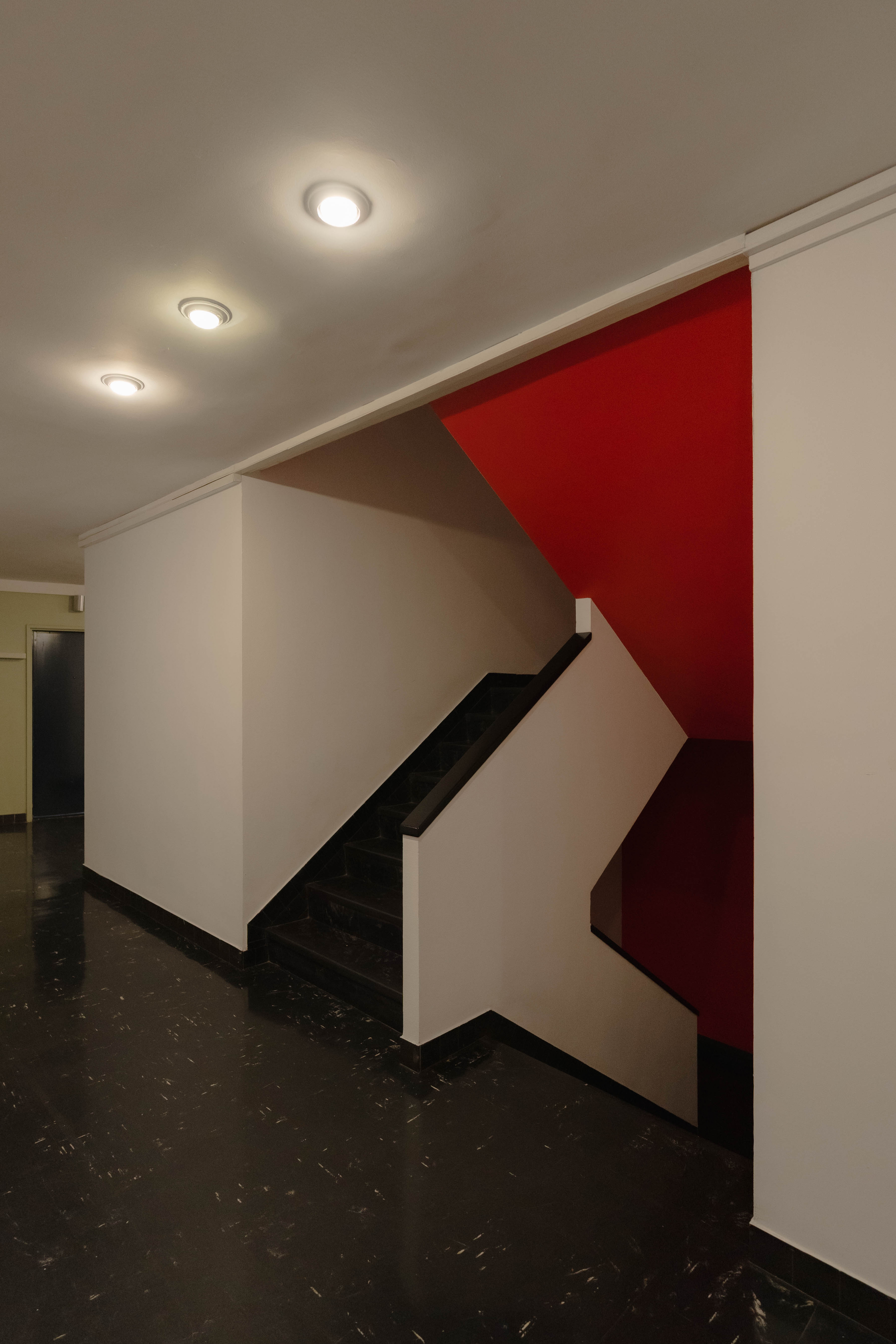 Escalier droit, mur rouge vif, sol marbre noir