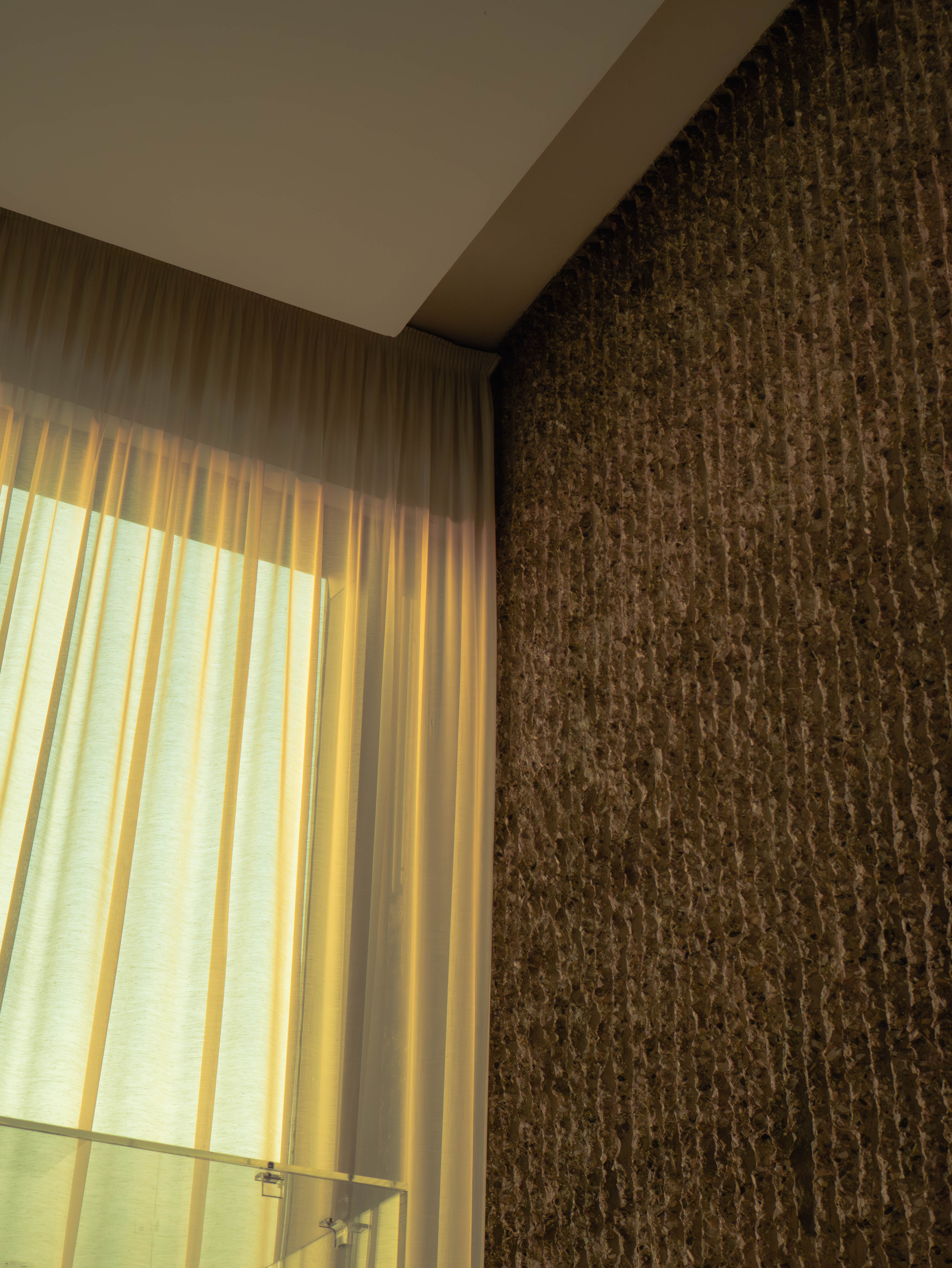 Fenêtre voilage ivoire, lumière dorée, mur pierre de lave