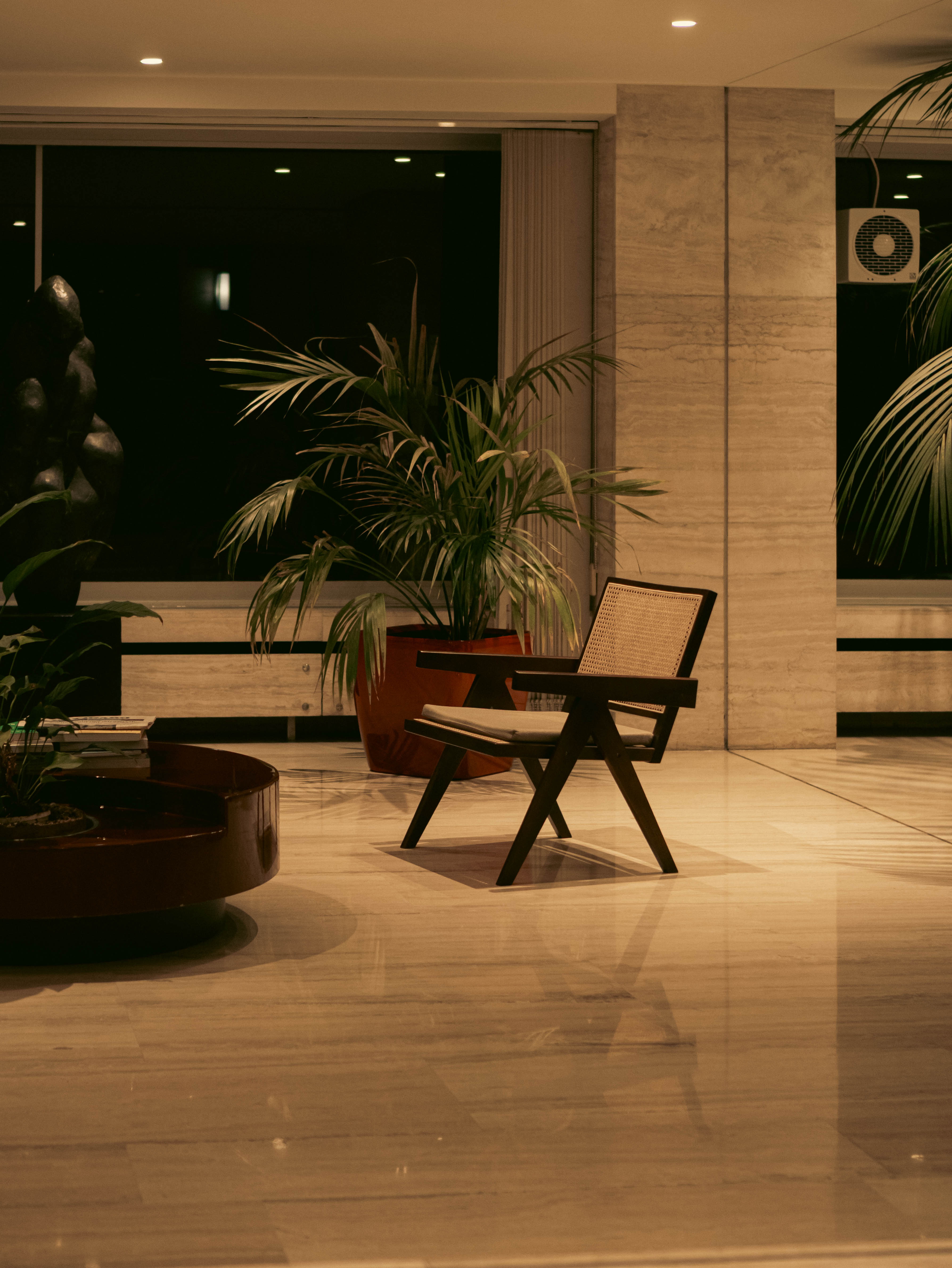 Lobby nocturne travertin clair, chaise cannée, palmier terracotta