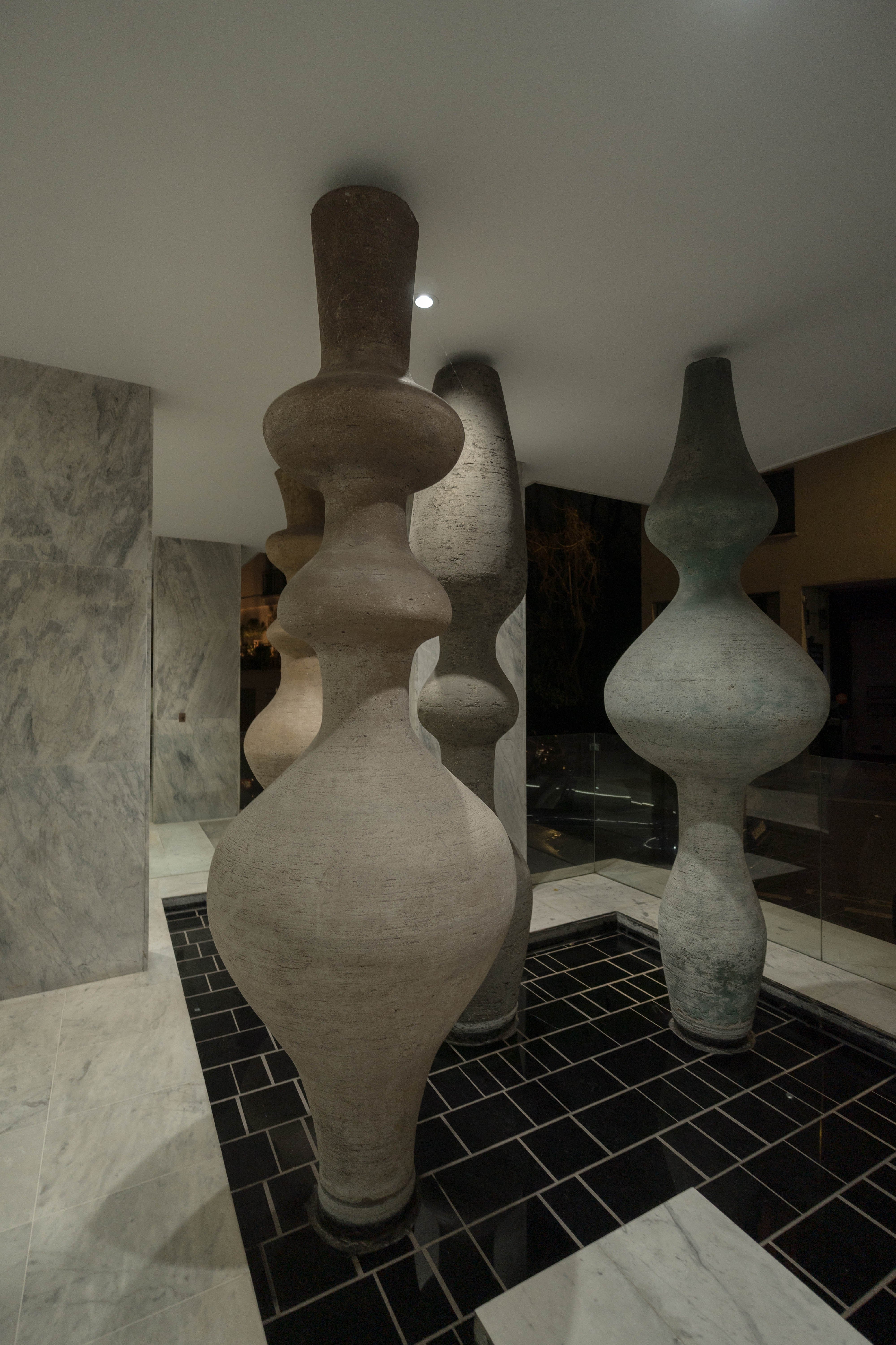 Sculptures céramique texturée, vases sinueux empilés, carrelage noir