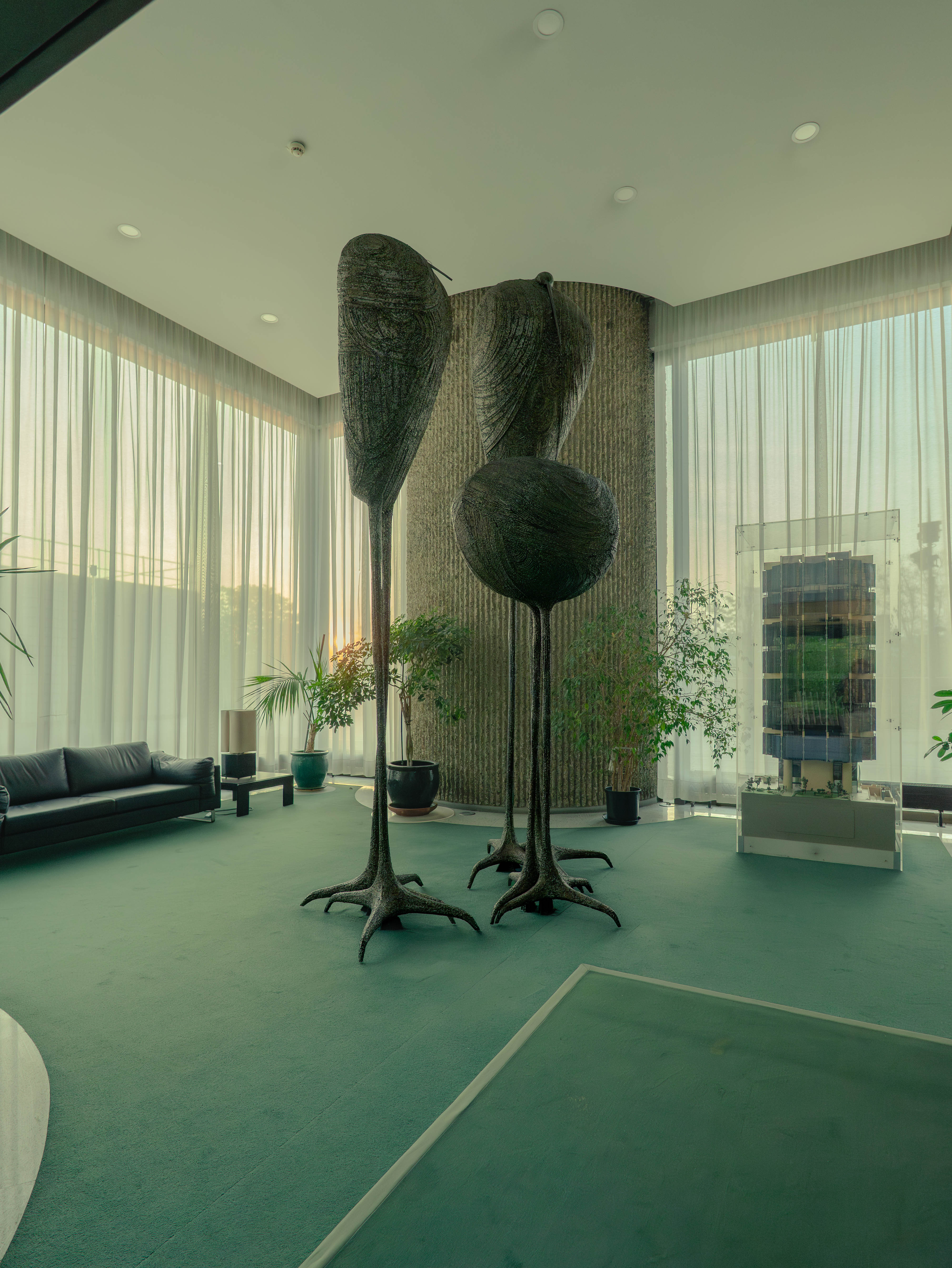 Hall sculptures oiseaux métalliques, moquette vert menthe, contre-jour