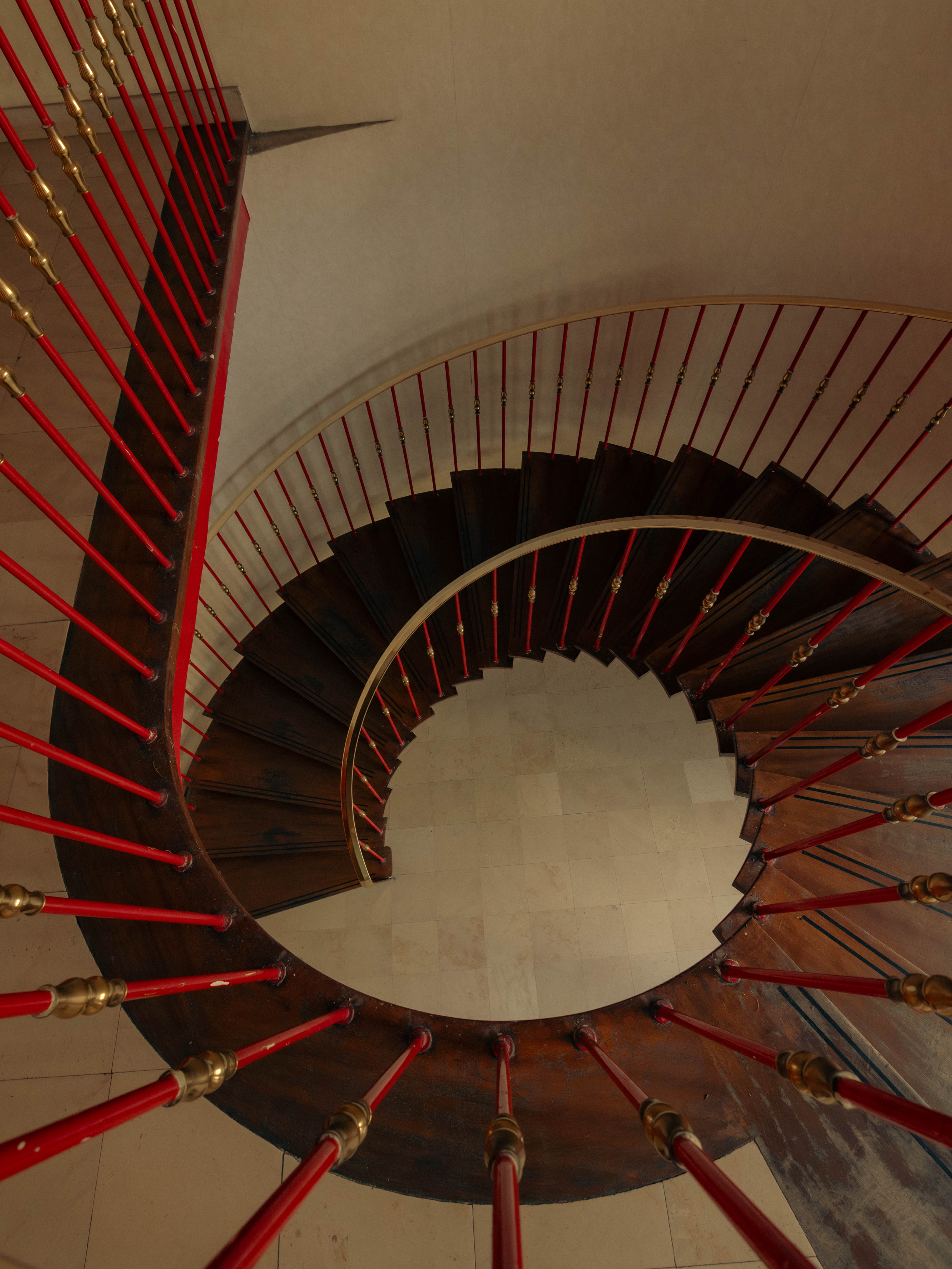 Vue plongeante escalier hélicoïdal bois foncé, balustres rouges et dorés