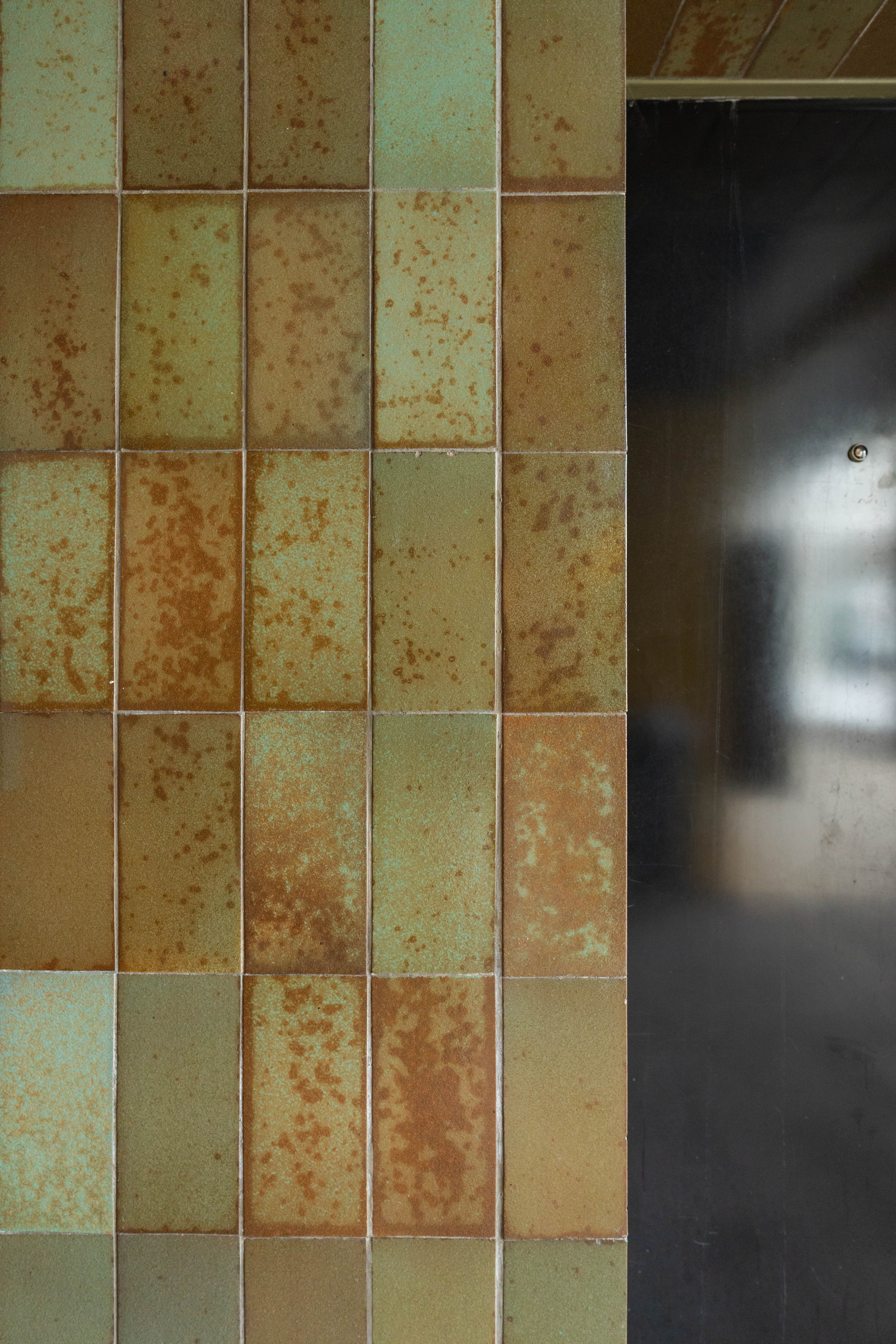 Gros plan carreaux céramique vert sauge et rouille, texture picturale