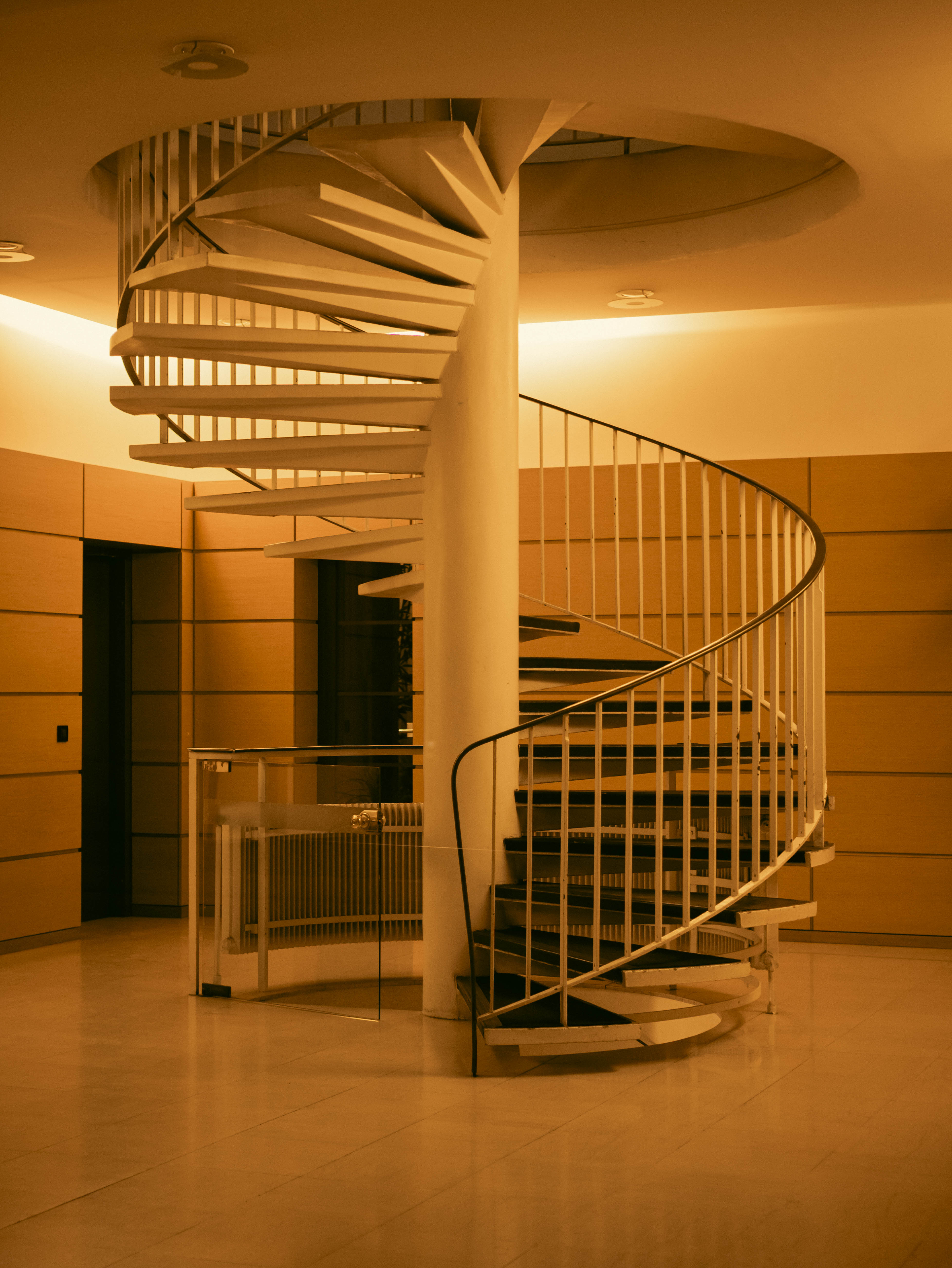 Escalier hélicoïdal blanc, éclairage orange très chaud, murs ocre