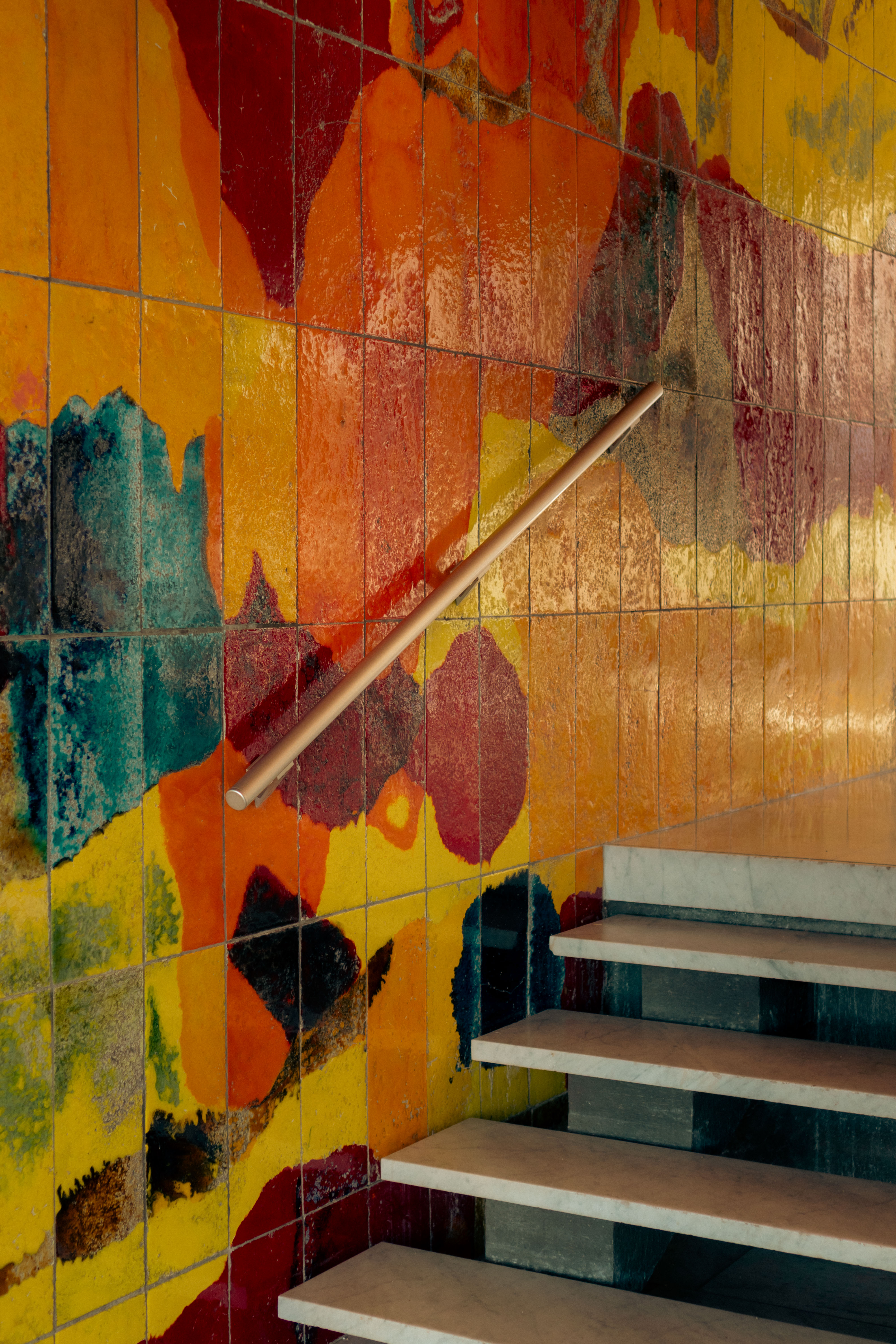 Cage escalier marbre blanc, rampe cuivre, carreaux émaillés orange et rouge