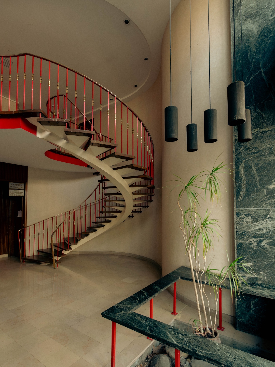 Hall — escalier hélicoïdal, rampe rouge, marbre vert
